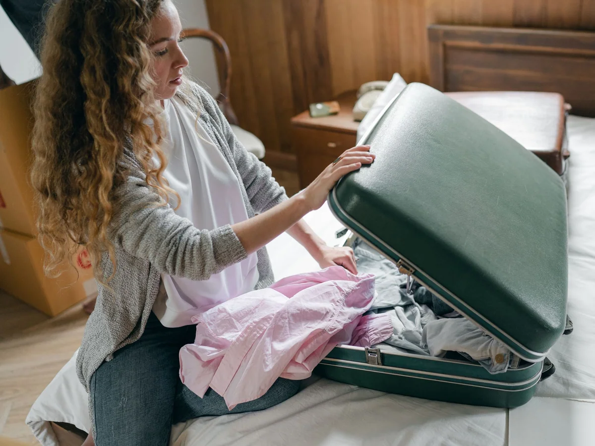 Woman packing a compact travel beauty pouch into a carry-on suitcase